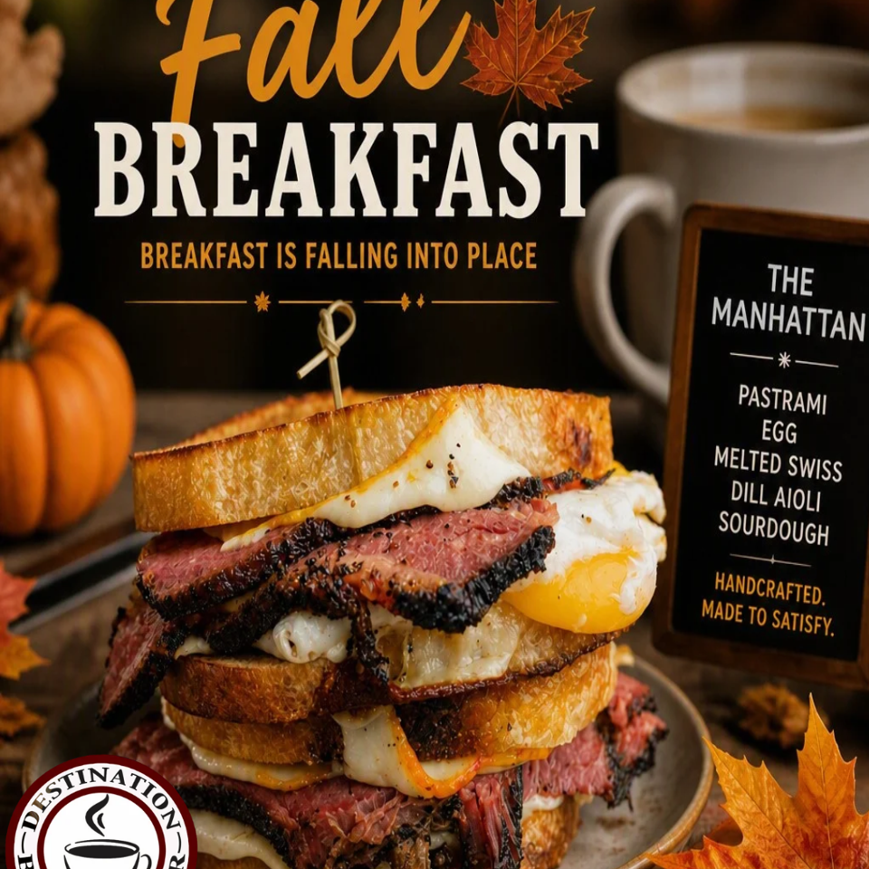 Stacked pastrami, egg, melted Swiss, and dill aioli sourdough sandwich beside coffee, pumpkins, and autumn leaves.